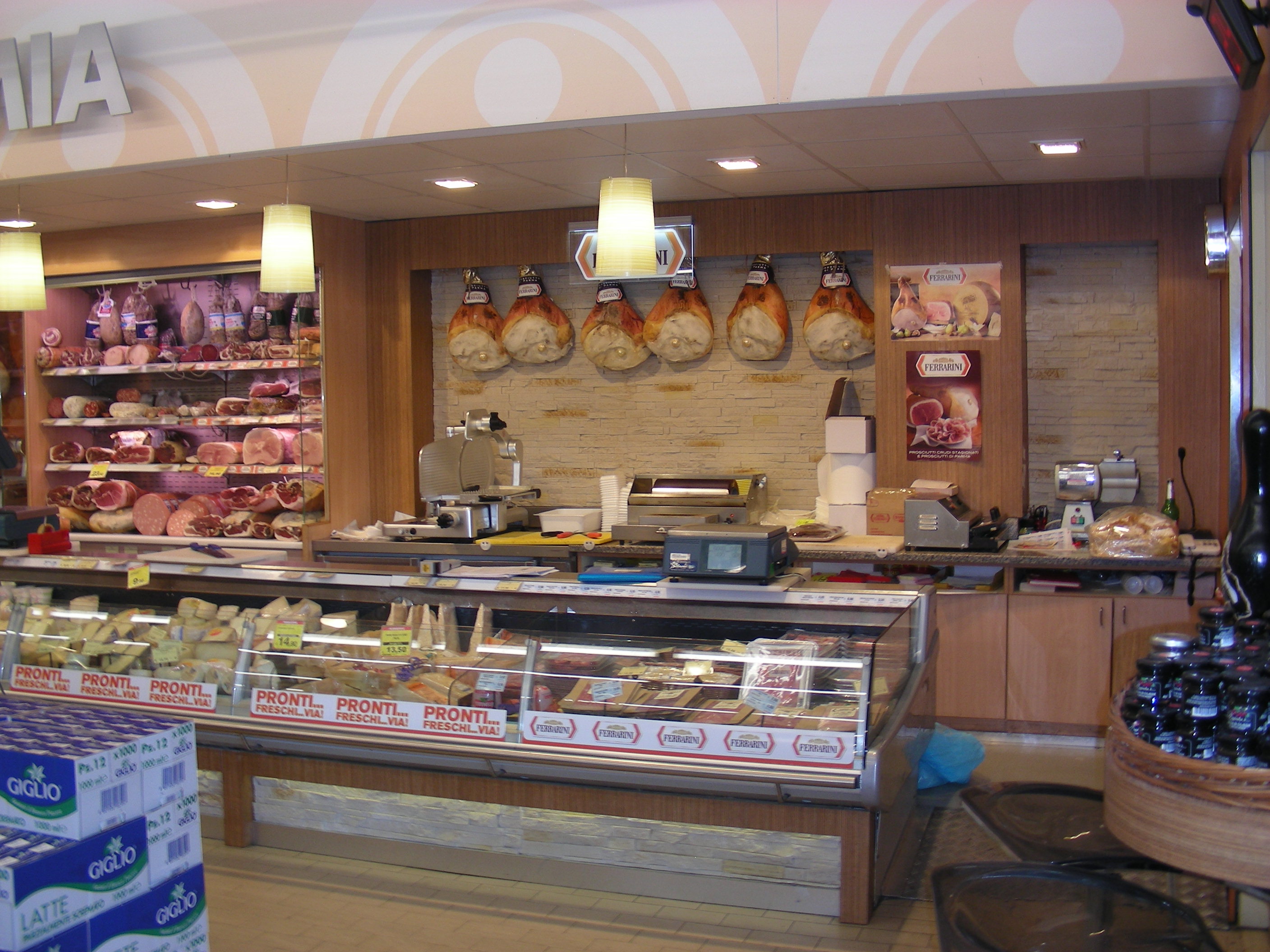 Allestimento reparto gastronomia, caratterizzato da un design caldo che richiama la tradizione, bancone refrigerato in vetro, retrobanco in legno, pareti in pietra chiara.